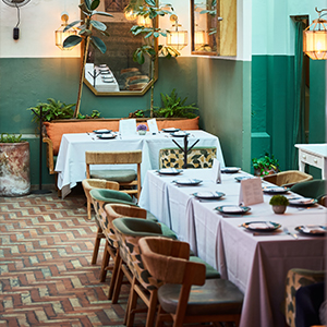 Interior de un restaurante con mesas blancas y verdes, decoración acogedora y plantas en el entorno.
