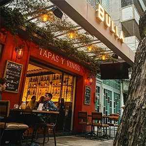 Exterior del restaurante Bulla, con letrero iluminado, ambiente acogedor y mesas al aire libre.