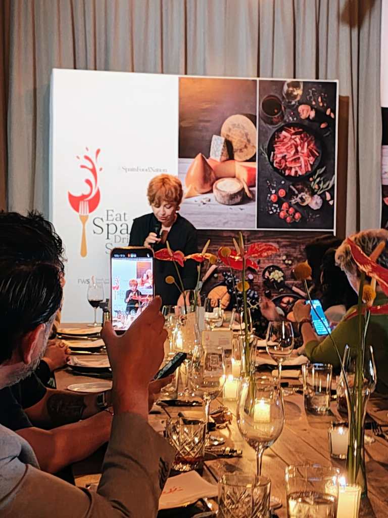 Un evento gastronómico con una presentación sobre comida y vino en una mesa decorada con flores, velas y copas.