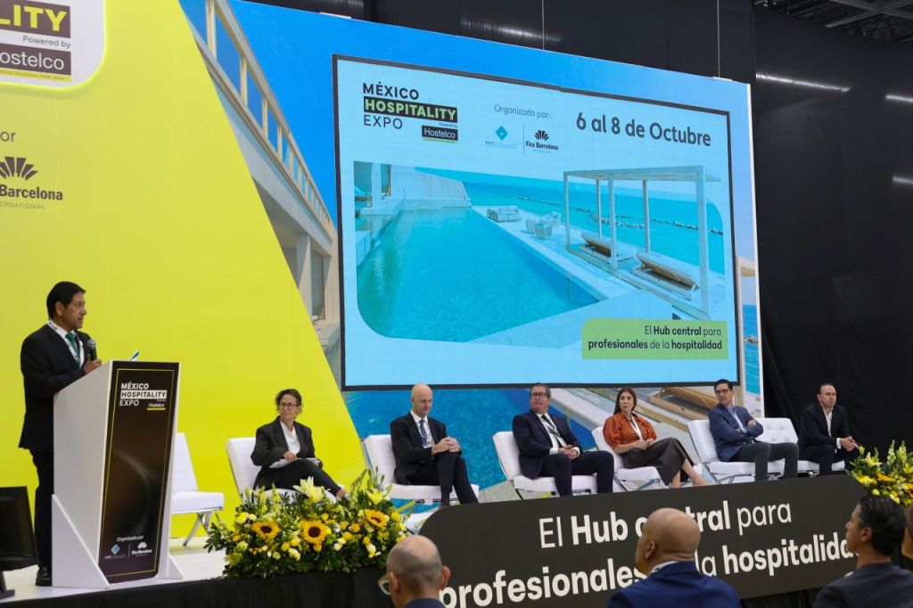 Conferencia en la Expo de Hospitalidad de México, mostrando a un ponente hablando frente a una pantalla grande con información del evento, que se llevará a cabo del 6 al 8 de octubre.